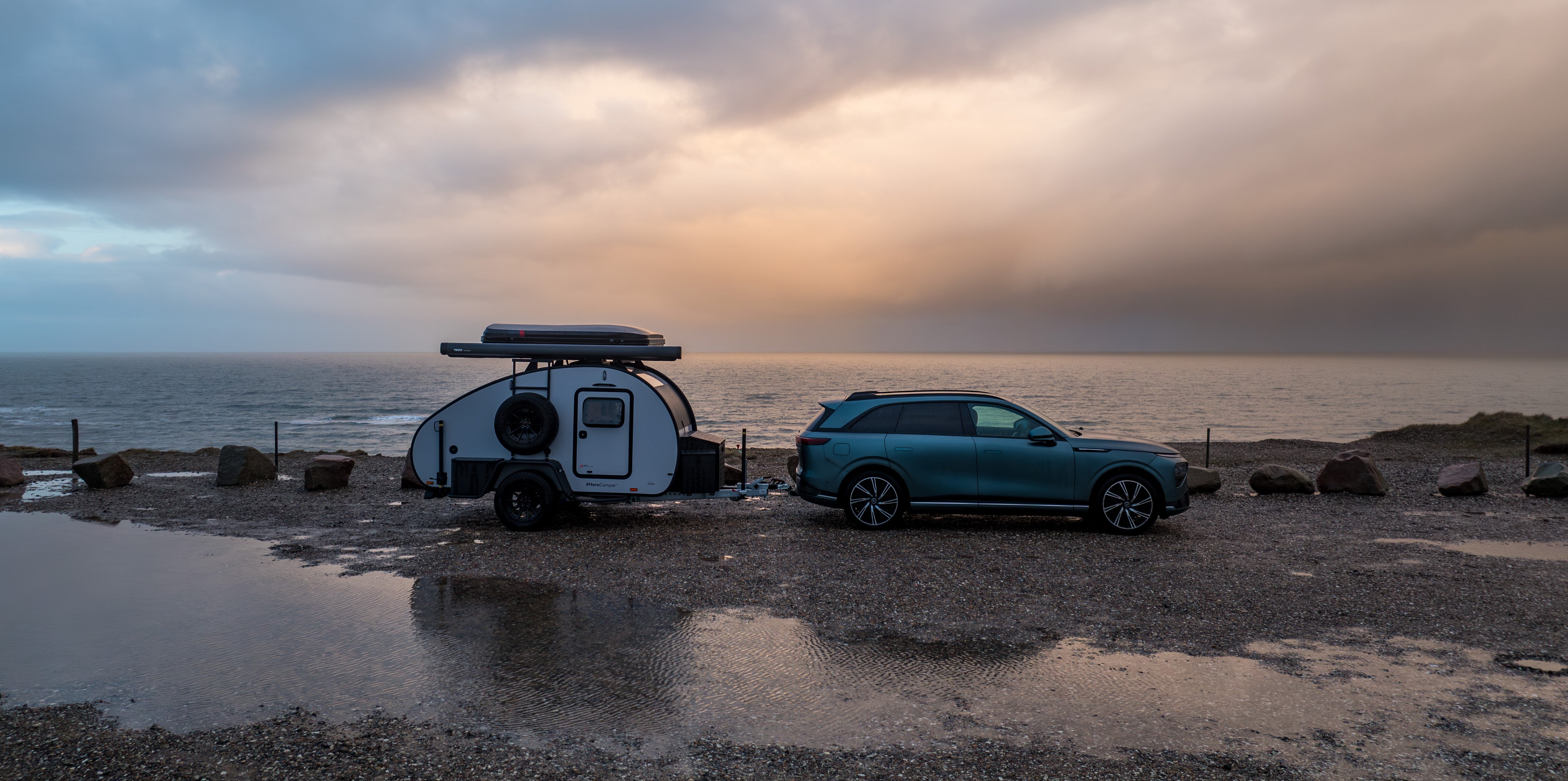 Minicaravan achter een elektrische trekauto. Geparkeerd aan de kustlijn.